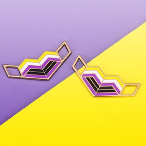 Könnte beinhalten: Zwei goldfarbene Pins mit einem Chevron-Design in den Farben der Non-Binary-Pride-Flagge: Gelb, Weiß, Lila und Schwarz.