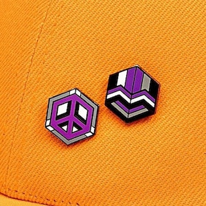 May include: Two enamel pins on a yellow baseball cap. The pins are both geometric shapes with purple, white and black accents. One pin is a peace sign and the other is a stylised letter W.