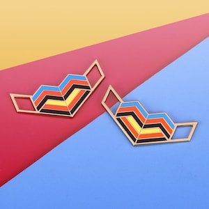 May include: Two gold-colored metal geometric shapes with a layered design. The shapes are painted with red, yellow, black, and blue enamel. The shapes are on a background of yellow, red, and blue.