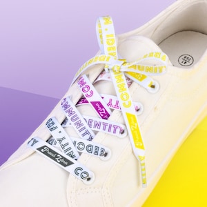 Puede incluir: Zapatillas blancas de lona con cordones amarillos y morados que tienen las palabras "Community", "Identity", "Freedom", "Proud Zebra" y "M. Identity" impresas en ellos.