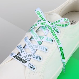 May include: White canvas sneakers with green and white shoelaces that have the words "COMMUNITY", "IDENTITY", "FREEDOM", and "Proud Zebra" printed on them.