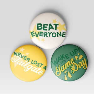 May include: Three round buttons with green and yellow text on a white background. The first button says "Beat Everyone" with yellow stars. The second button says "Never Lost A Tailgate" with yellow stars. The third button says "Wake Up! It's Game Day" with yellow droplets.