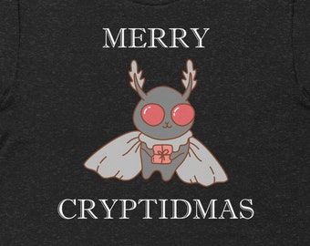 May include: A dark heather grey t-shirt with a white graphic of a moth with red eyes holding a gift. The text "Merry Cryptidmas" is printed in white below the moth.