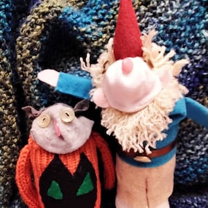 May include: Two handmade sock puppets, one a gnome with a red hat and a white beard, the other a cat with a black and green design on an orange sweater.