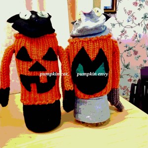 May include: Two knitted sock puppets dressed as pumpkins. One is black with an orange pumpkin face and the other is gray with a black pumpkin face. The text "pumpkin cat" and "pumpkin envy" is written on the puppets.