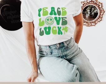 May include: White t-shirt with a green and white graphic that says "Peace Love Luck" with a shamrock and a smiley face with hearts for eyes.