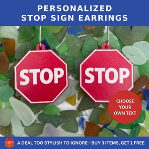 Puede incluir: Un par de pendientes de señal de stop rojos con letras blancas. Los pendientes están sobre un lecho de vidrio de mar de colores. El texto en los pendientes dice "STOP". El texto "CHOOSE YOUR OWN TEXT" también es visible en la imagen.
