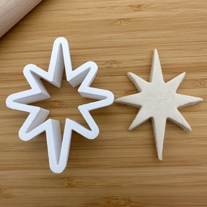 May include: A white plastic cookie cutter in the shape of a star, next to a white star-shaped cookie.