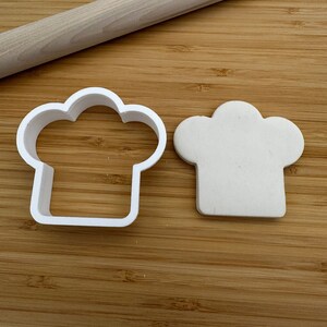 May include: White plastic chef hat cookie cutter with a piece of white modeling clay pressed into the cutter.