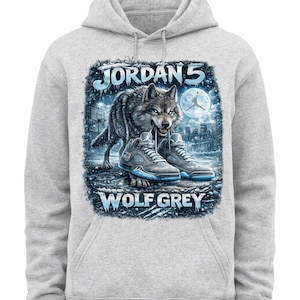Könnte beinhalten: Hellgrauer Kapuzenpullover mit einer Grafik eines Wolfes, Wolf Grey Jordan 5 Sneakern und dem Text "JORDAN 5" und "WOLF GREY". Das Design beinhaltet eine Stadtlandschaft und einen Vollmond.