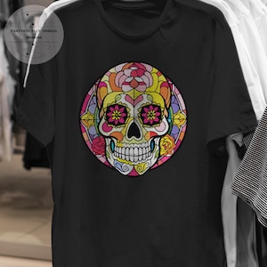 May include: Black t-shirt with a vibrant sugar skull design. The skull is adorned with floral and geometric patterns in yellow, pink, and blue. The shirt features the text "Fantastically-Unreal Designs".