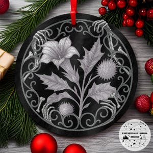 Puede incluir: Adorno navideño redondo negro con un diseño floral detallado en escala de grises. El adorno presenta una flor grande, hojas y cardos, rodeados por un borde decorativo con manos esqueléticas. Se adjunta una cinta roja. Decoración navideña única.