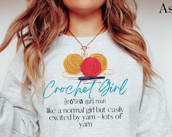 May include: A gray sweatshirt with the text "Crochet Girl [krō'SHā gurl] noun like a normal girl but easily excited by yarn - lots of yarn" printed on it. The sweatshirt has a graphic of three balls of yarn, two yellow and one red, with a crochet hook.