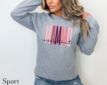 Puede incluir: Sudadera gris deportiva con el texto "MAMMO assistant" en letras rosas y burdeos. La palabra "assistant" está en cursiva. La sudadera se combina con pantalones cortos vaqueros.