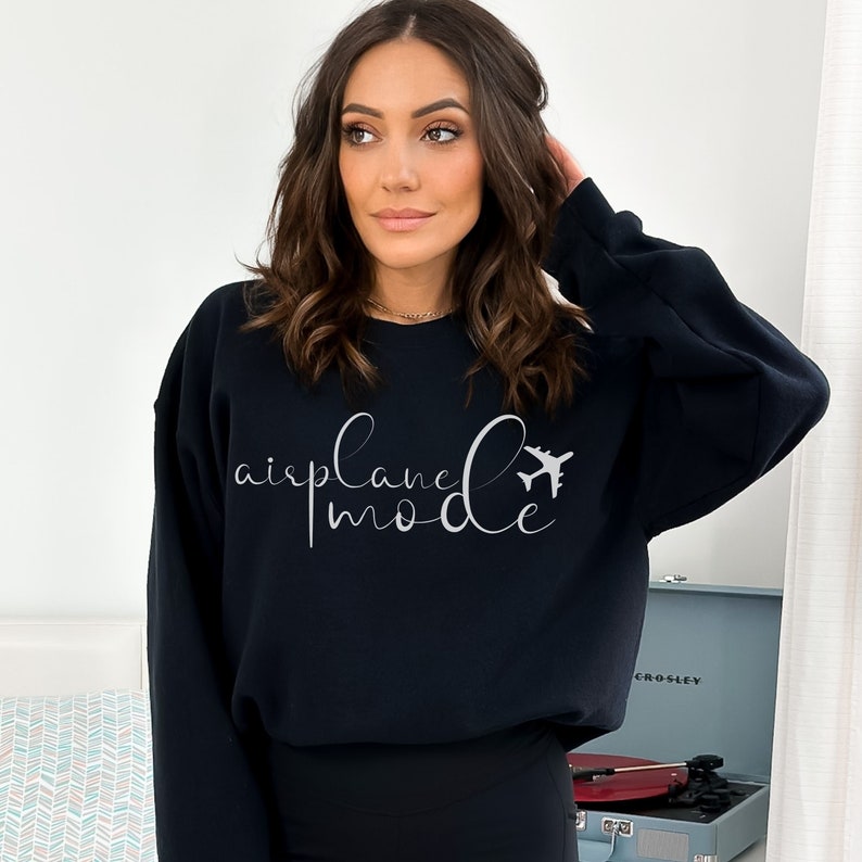 May include: A black sweatshirt featuring the text "airplane mode" in a cursive script, accompanied by a small airplane illustration. The sweatshirt is plain and has a round neck.