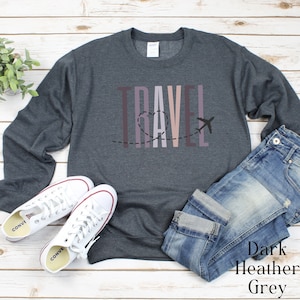 May include: A dark heather grey sweatshirt with the word "TRAVEL" printed in vertical rainbow colors with a heart and airplane graphic.