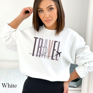 May include: White sweatshirt with the word "TRAVEL" printed in colorful vertical stripes. A heart with a dotted line and a small airplane are above the word.