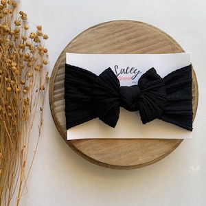 May include: Black ribbed knotted headband with the text "Lacy Bow Co."