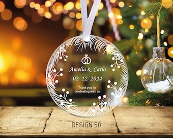 Könnte beinhalten: Ein runder, transparenter Weihnachtsbaumschmuck mit einem weißen Design aus einem Kranz mit Beeren und dem Text "Amelia & Carlo 02.12.2024 Thank you for celebrating with us" und dem Text "DESIGN 50" unter dem Ornament.