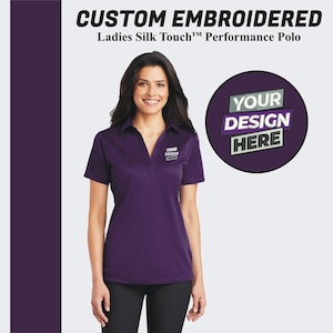 May include: Purple performance polo shirt with a v-neck collar and short sleeves. The shirt has "YOUR DESIGN HERE" embroidered on the left chest.