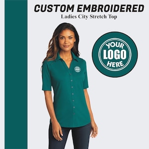 May include: A teal blue, short-sleeved, button-down shirt with a v-neck collar. The shirt has a small embroidered logo on the left chest. The text "YOUR LOGO HERE" is in a circle on the right side of the image.