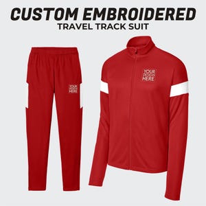 May include: Red travel track suit with white accents. The jacket has a zipper closure and white stripes on the sleeves. The pants have white stripes on the sides. The text "YOUR DESIGN HERE" is embroidered on the jacket.
