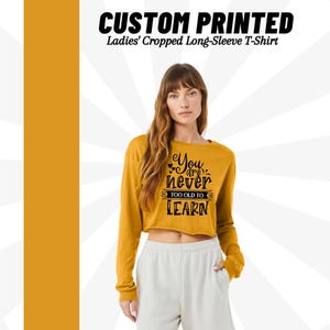 Może przedstawiać: Ż&oacute;łty, kr&oacute;tki t-shirt z długim rękawem w kolorze musztardowym z nadrukiem "You are never too old to learn" w kolorze czarnym.