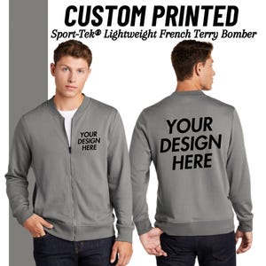 May include: A gray zippered bomber jacket with long sleeves. The jacket has "YOUR DESIGN HERE" printed on the front and back.