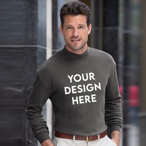 May include: A dark gray long-sleeved sweatshirt with a mock neck and the text "YOUR DESIGN HERE" in white. The sweatshirt is paired with light-colored pants and a brown belt.
