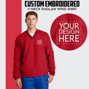 May include: Red V-neck wind shirt with long sleeves and a custom embroidery area. The text "YOUR DESIGN HERE" is displayed on the shirt.