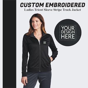 May include: Black track jacket with a zipper and striped sleeves. The jacket has a small embroidered area on the left chest that says "YOUR DESIGN HERE".