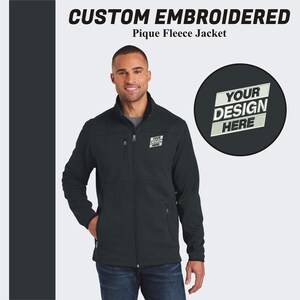 May include: A black fleece jacket with a zipper closure and two pockets. The jacket has a  "YOUR DESIGN HERE" embroidered patch on the left chest.