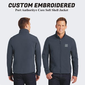 May include: A dark blue soft shell jacket with a zipper closure and a stand-up collar. The jacket has a small embroidered logo on the chest that says "YOUR DESIGN HERE".