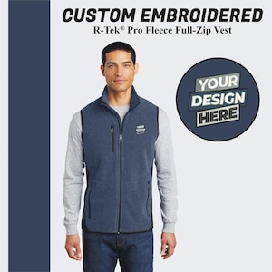 Peut inclure: Un gilet en polaire bleu avec une fermeture éclair et deux poches. Le gilet a une bordure noire et un petit patch brodé qui dit "YOUR DESIGN HERE".