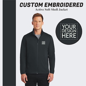 May include: A black soft shell jacket with a zipper closure. The jacket has a mock neck and two pockets. The text "YOUR DESIGN HERE" is embroidered on the left chest of the jacket.
