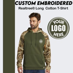 May include: A green long-sleeve hooded sweatshirt with a camouflage pattern on the sleeves. The sweatshirt has a pocket on the front and a small embroidered logo on the left chest that says "YOUR LOGO HERE".