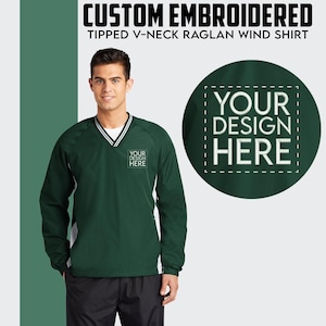 May include: A green windbreaker with white tipped sleeves and a v-neck. The jacket has a white stripe across the v-neck and a small embroidered logo that says "YOUR DESIGN HERE".