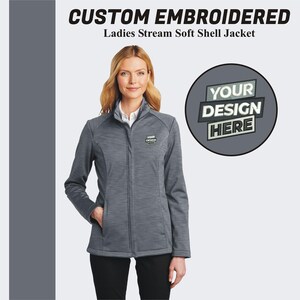 May include: A gray soft-shell jacket with a zipper closure. The jacket has a stand-up collar and two front pockets. The text "YOUR DESIGN HERE" is displayed on a circle in the upper right corner of the image.