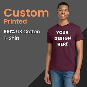 May include: A maroon t-shirt with the text "YOUR DESIGN HERE" in white. The image also includes the text "Custom Printed" and "100% US Cotton T-Shirt" in orange and white. A person is wearing the t-shirt.