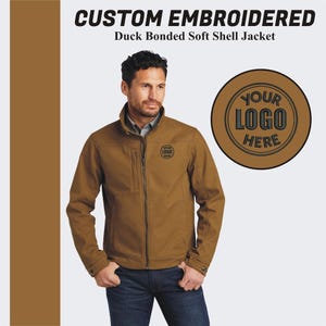 Peut inclure: Une veste en softshell marron avec une fermeture éclair et un logo brodé sur la poitrine gauche. Le texte "YOUR LOGO HERE" est affiché dans un cercle sur le côté droit de l'image.