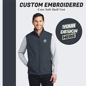 May include: A dark blue soft shell vest with a zipper closure. The vest has a mock neck and two front pockets. The vest is embroidered with the text "YOUR DESIGN HERE" on the left chest.