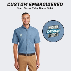 May include: A blue denim short-sleeve shirt with a button-down collar. The shirt has a pocket on the left chest with the text "YOUR DESIGN HERE" embroidered on it.