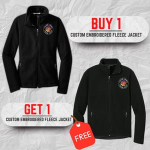 May include: Two black custom embroidered fleece jackets are displayed. Each jacket has a zipper closure and a logo on the chest. The image includes text that reads "BUY 1" and "GET 1" with the words "CUSTOM EMBROIDERED FLEECE JACKET". A red tag says "FREE".