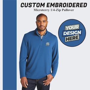 May include: A blue 1/4-zip pullover with a mock neck and long sleeves. The pullover has a small embroidered logo that says "YOUR DESIGN HERE".