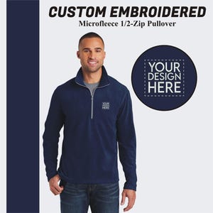 May include: A navy blue microfleece 1/2-zip pullover with a zipper on the front. The pullover has a mock neck and a small embroidered design on the left chest that says "YOUR DESIGN HERE".