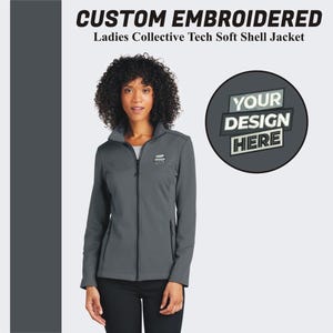 May include: A gray soft shell jacket with a zipper closure. The jacket has a mock neck and two front pockets. The text "YOUR DESIGN HERE" is embroidered on the jacket.