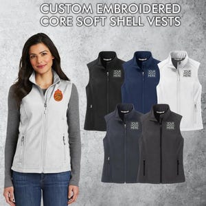 May include: Six soft shell vests in different colors, including black, navy, gray, and white. Each vest has a zipper closure and two pockets on the sides. The vests are embroidered with the text "YOUR DESIGN HERE".