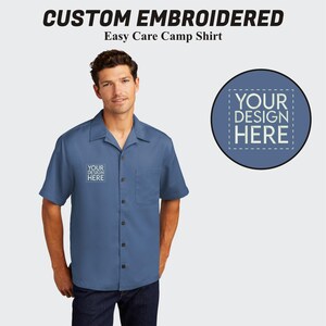 May include: A blue short-sleeved button-down shirt with a white embroidered design that says "YOUR DESIGN HERE". The shirt is a camp shirt and is made of easy care fabric.