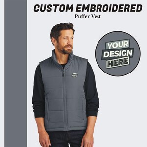 May include: A gray puffer vest with a zipper closure. The vest has a quilted design and a small embroidered patch that says "YOUR DESIGN HERE".