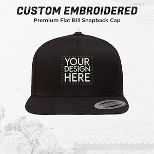 May include: Black flat bill snapback cap with a white embroidered square that says "YOUR DESIGN HERE".